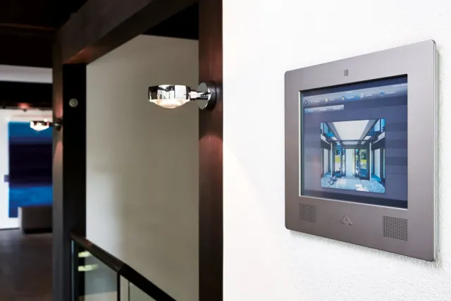 Edelstahl-Wandbedienfeld mit Touchdisplay einer Gebäudesteuerung neben einer Wandleuchte