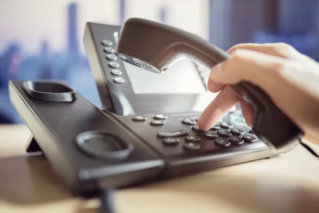Hand wählt an einem Tischtelefon